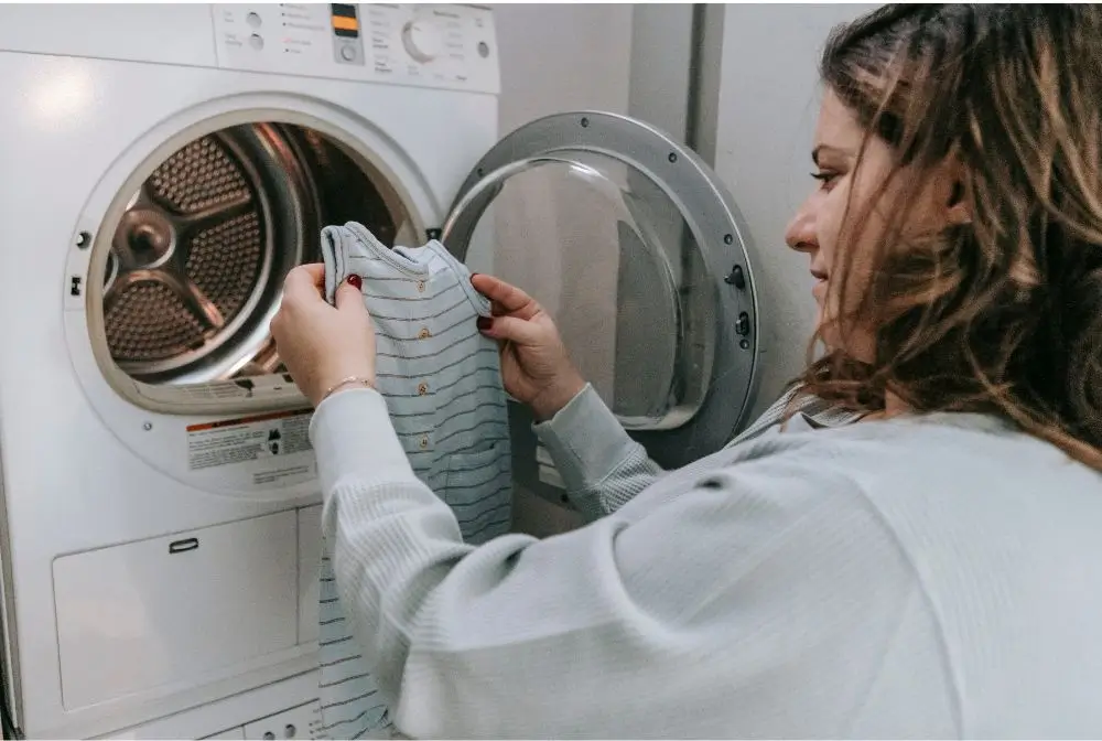 Como lavar enxoval bebê.imagem de mulher colocando roupade bebe na maquina de lavar roubar