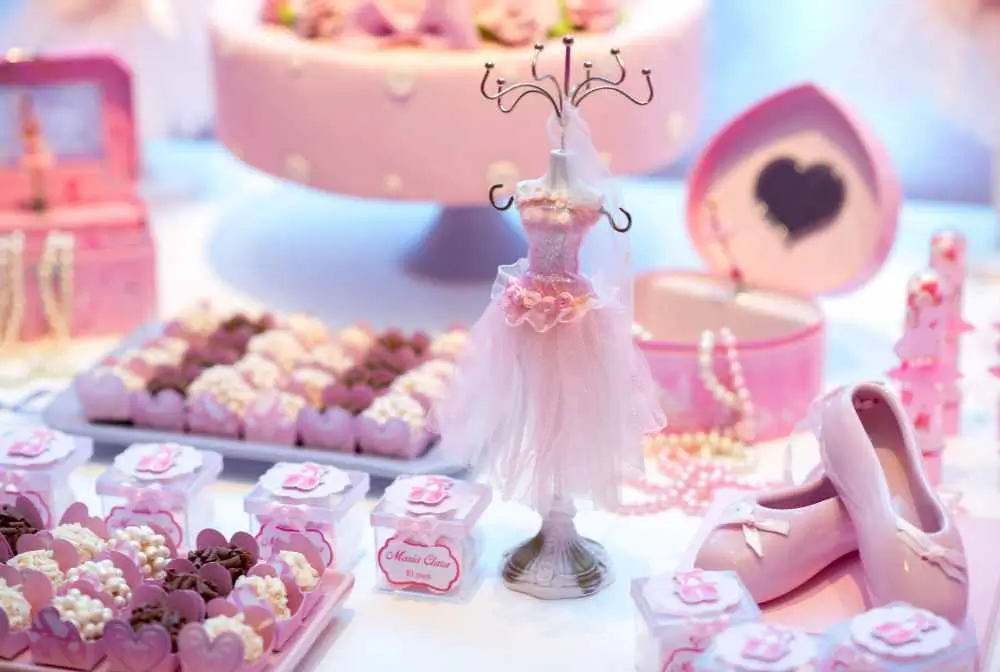 imagem de bolo e docinhos no tem ade princesa em uma mesa de festa com um mini vestido rosa ao centro da imagem