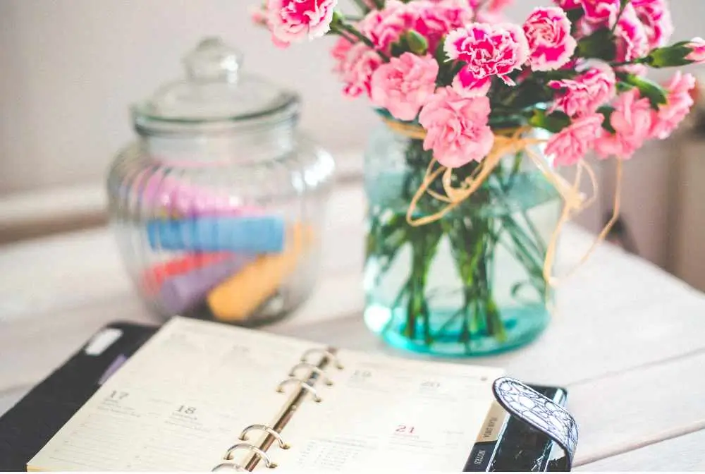 imagem de uma agenda aberta sob. mesa com flores e um pote de vidro com item de festa