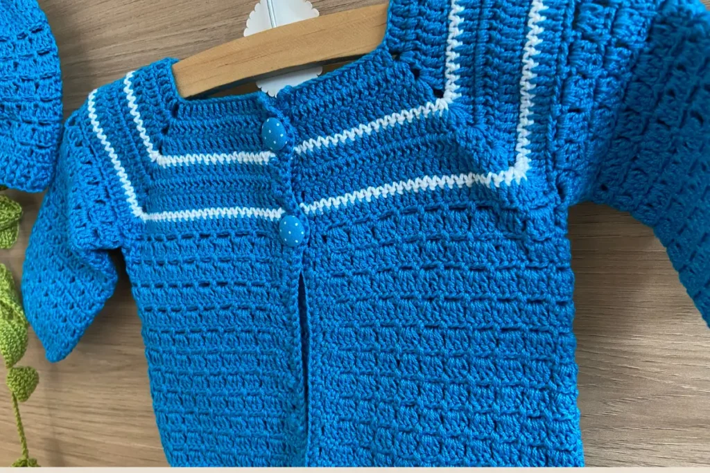 Detalhe dos botões forrados azuis com detalhes em bolinhas brancas do casaquinho de crochê para bebê, mostrando acabamento artesanal e facilidade para vestir